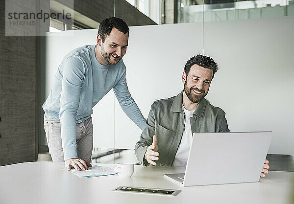 Lächelnde Geschäftskollegen diskutieren am Laptop im Büro