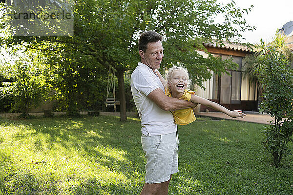 Playful father carrying daughter in backyard