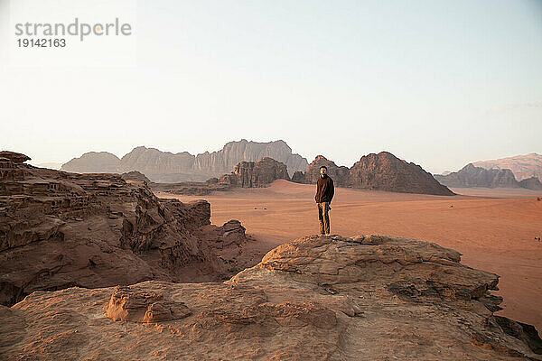 Young man standing on desert rock at sunset