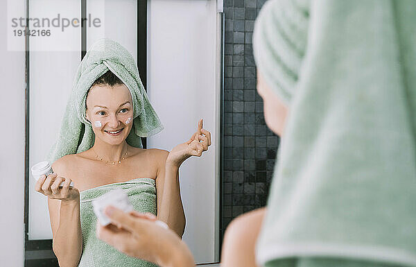 Smiling woman applying cream on face after shower