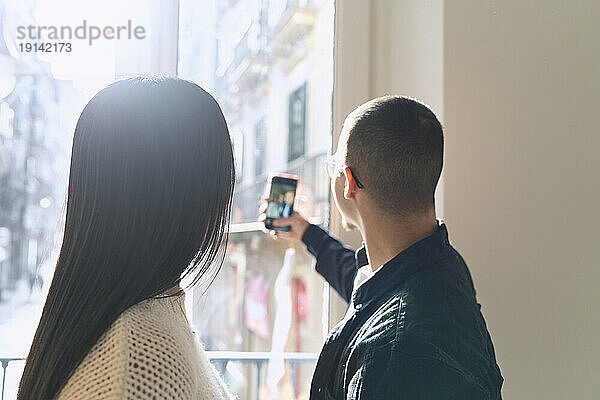 Paar macht Selfie mit Smartphone am heimischen Fenster