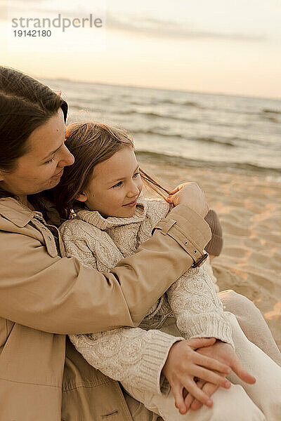 Lächelnde Mutter umarmt Tochter am Strand