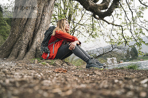 Hiker taking rest sitting near tree in forest