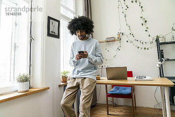 Junger Freiberufler nutzt Mobiltelefon im Heimbüro