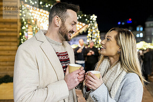 Glücklicher Mann und Frau mit Kaffeetasse auf dem Weihnachtsmarkt