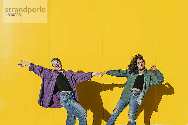 Fröhliches lesbisches Paar hält Händchen vor gelber Wand