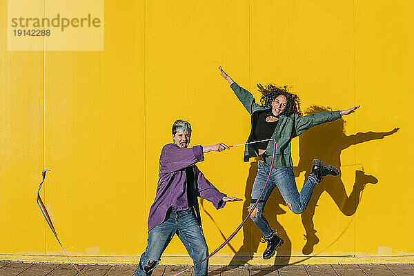 Glückliche Frau mit lesbischer Freundin springt vor gelbe Wand