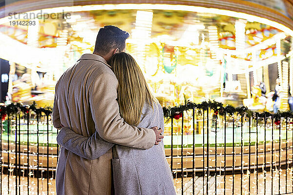 Couple hugging each other in front of carousel at Christmas market