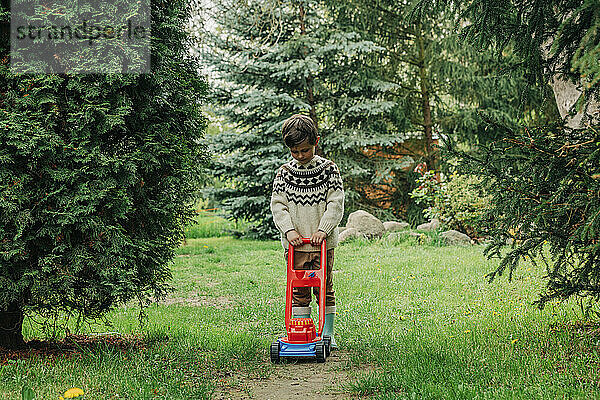 Junge spielt mit Spielzeugrasenmäher im Garten