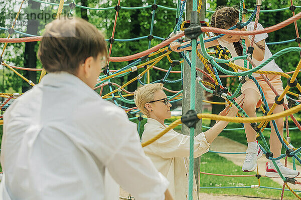 Lesbian mothers with daughter climbing jungle gym in playground
