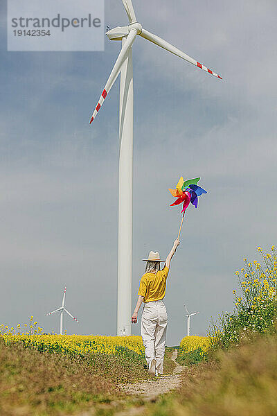 Frau hält buntes Windradspielzeug mit Windkraftanlage im Hintergrund