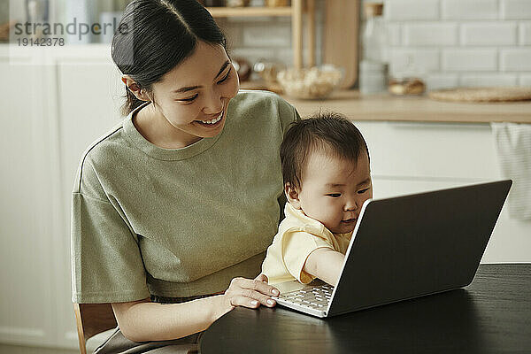 Happy freelancer mother with daughter using laptop at home