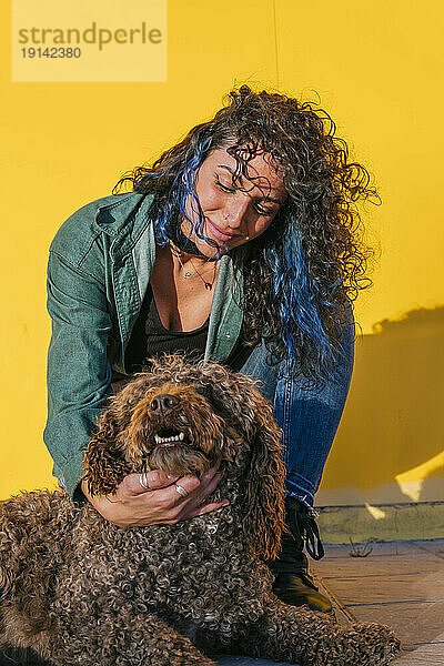 Woman with curly hair stroking water dog in front of yellow wall