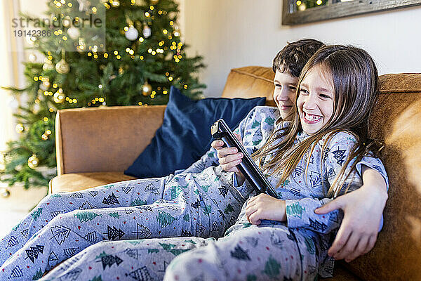 Glückliches Mädchen  das zur Weihnachtszeit zu Hause mit seinem Bruder fernsieht