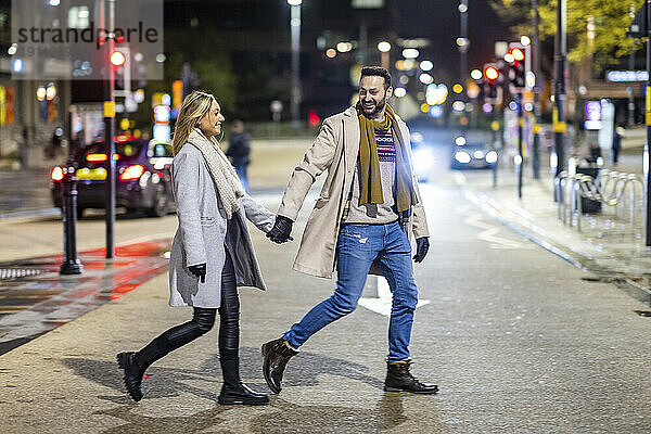 Glücklicher Mann hält Händchen mit Frau und überquert gemeinsam die Straße