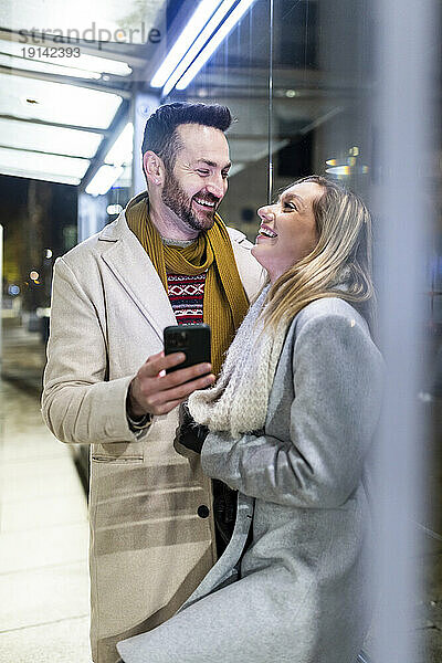Glücklicher Mann und Frau stehen mit Mobiltelefon