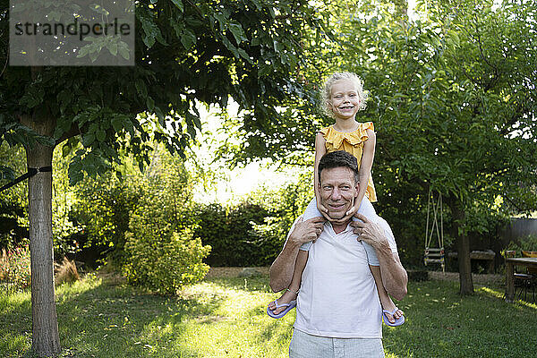 Glücklicher Vater trägt Tochter auf Schultern im Garten