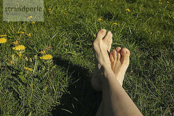 Frau mit gekreuzten Beinen im Gras an einem sonnigen Tag