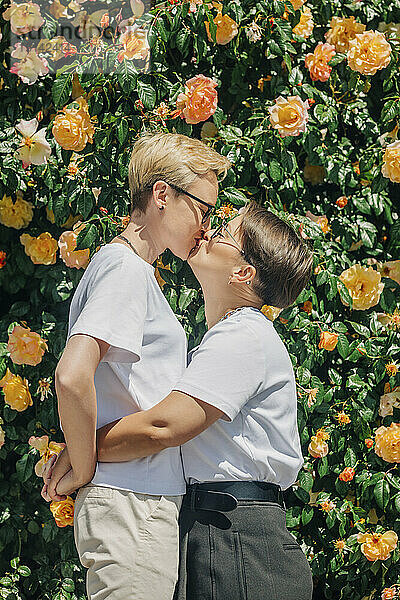 Lesbisches Paar küsst sich vor einer Wand mit Rosen