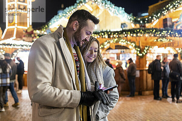 Junge Frau und Mann nutzen Smartphone auf dem Weihnachtsmarkt