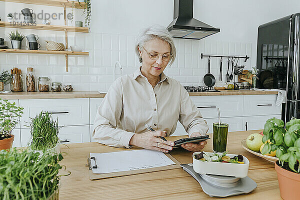 Reife Frau mit Tablet-PC in der heimischen Küche