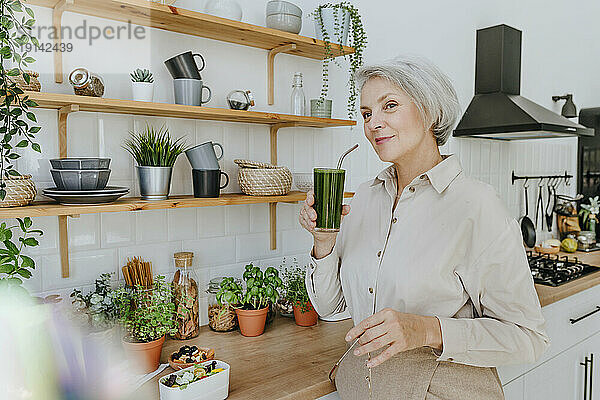 Lächelnde Frau trinkt Detox-Saft in der heimischen Küche