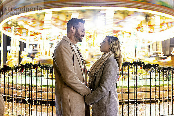 Paar hält sich an den Händen und steht vor dem Karussell auf dem Weihnachtsmarkt