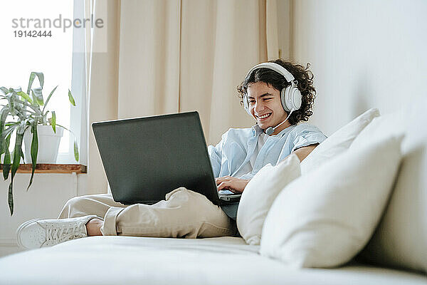 Fröhlicher Junge mit Headset und Laptop auf der heimischen Couch