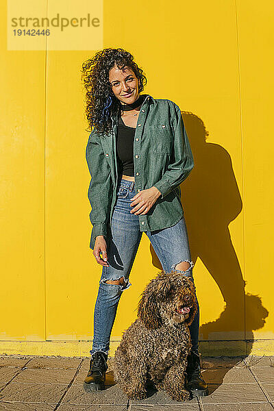 Lächelnde Frau steht mit Wasserhund vor gelber Wand