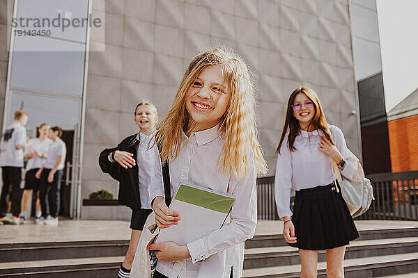 Blond girl standing in front of school building with friends in background