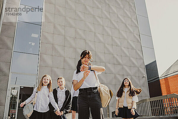 Mädchen überprüft die Zeit mit Freunden  die vor dem Schulgebäude stehen
