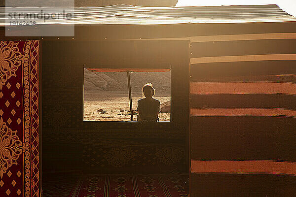 Young woman standing by tent in desert camp at sunset
