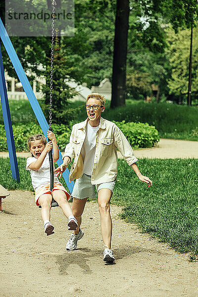 Fröhliche Mutter mit Tochter schaukelt auf dem Spielplatz