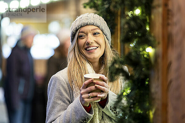 Glückliche junge Frau mit Kaffeetasse auf dem Weihnachtsmarkt