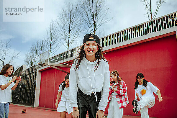 Lächelndes Teenager-Mädchen  das mit Freunden auf dem Spielplatz spielt