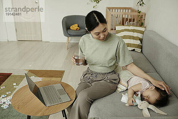 Freelancer mother stroking daughter sleeping on sofa at home