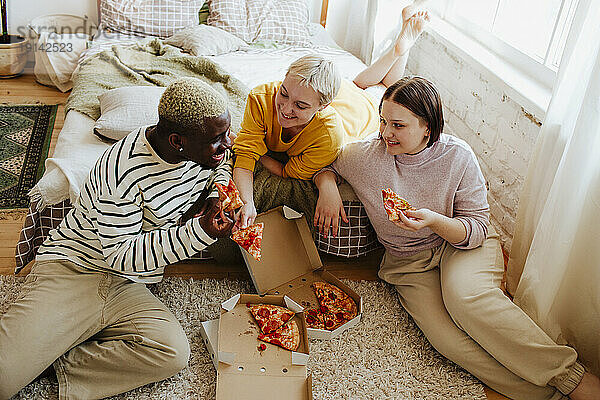 Young friends enjoying pizza sitting on bed at home