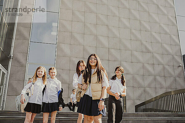 Smiling schoolgirl standing with friends in front of building