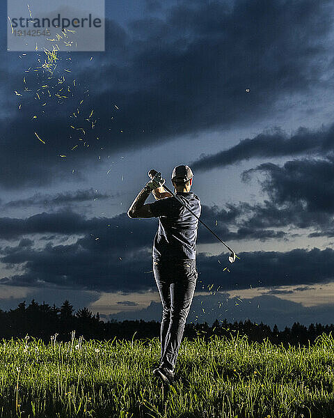 Man playing golf standing on grass facing sky at dusk