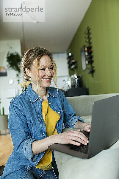 Freiberufler im Jeanshemd arbeitet mit Laptop auf der Couch