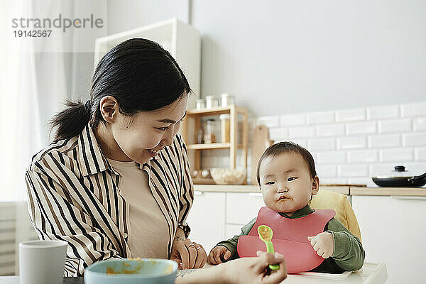 Smiling woman feeding fruit puree to daughter at home