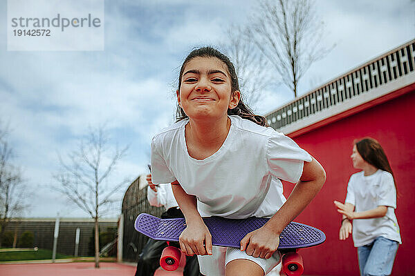 Lächelndes Teenager-Mädchen hält Skateboard auf dem Spielplatz
