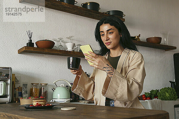 Junge Frau benutzt Smartphone und genießt gebrühten Kaffee am Tisch