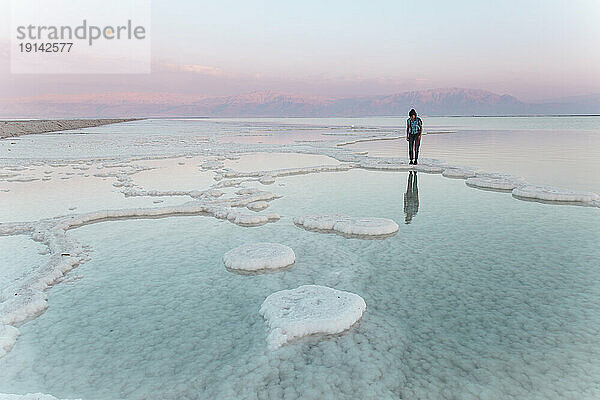Junge Frau steht bei Sonnenuntergang auf Salzformationen im Toten Meer
