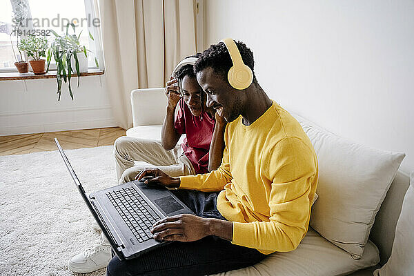 Lächelnde junge Freunde  die zu Hause einen Laptop teilen