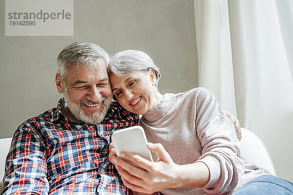 Lächelndes älteres Paar  das zu Hause ein Smartphone benutzt