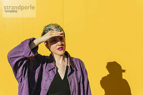 Frau schützt ihre Augen vor der gelben Wand vor Sonnenlicht