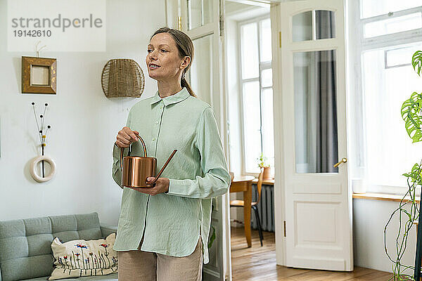 Mature woman standing with watering can at home