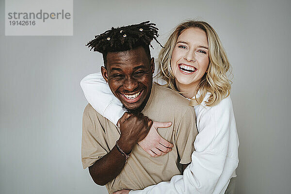 Cheerful young couple with arm around laughing against gray background