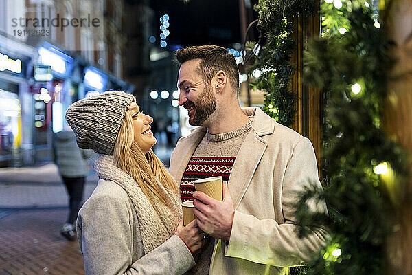 Glückliches Paar steht mit Kaffeetasse auf dem Weihnachtsmarkt